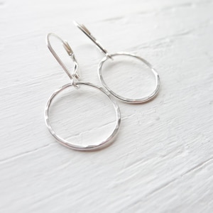 May include: A pair of silver hammered hoop earrings with leverback closures.