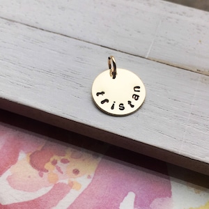 May include: Gold-toned round charm with the name "Tristan" engraved around the edge.