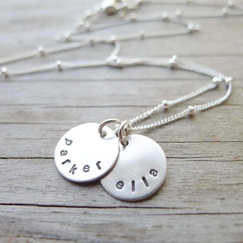 sterling silver small disc charm necklace with lowercase names - one on each 1/2" charm across the bottom of the charms. Necklace is made of delicate dainty beaded chain