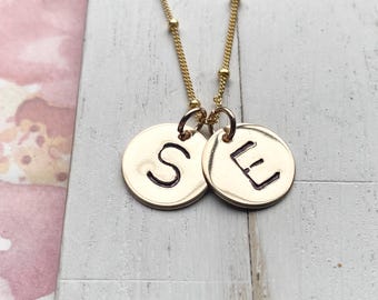 May include: Gold necklace with two round pendants, one with the letter 'S' and the other with the letter 'E'.