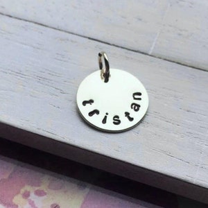 May include: Silver charm with the name "Tristan" engraved around the edge.
