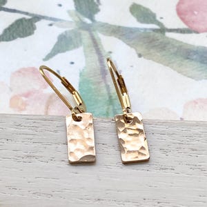 May include: A pair of gold hammered rectangle earrings with a simple hoop design.