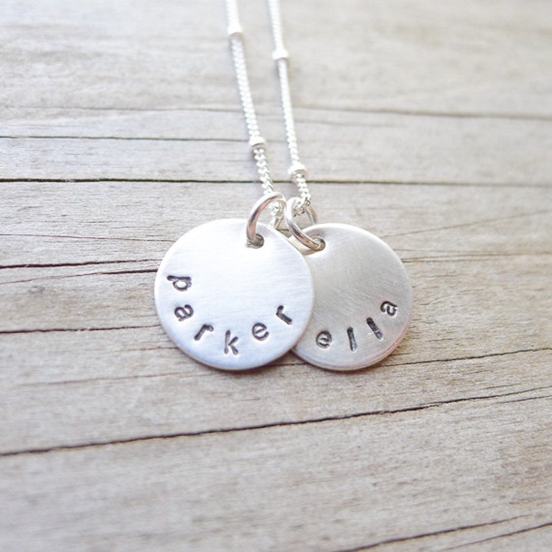 May include: A silver necklace with two round pendants, one engraved with the name "Parker" and the other with the name "Ella".
