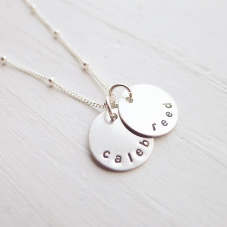 May include: Silver necklace with two round pendants, one with the name "Caleb" and the other with the name "Reed".