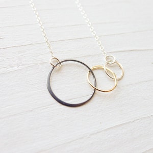 May include: A silver chain necklace with three interlocking circles. The largest circle is black, the middle circle is silver, and the smallest circle is gold.