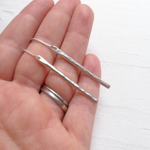 Puede incluir: Un par de pendientes de barra martillados de plata con una cadena delicada.