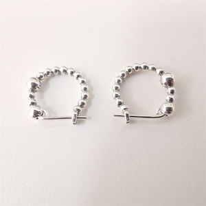 May include: A pair of silver hoop earrings. Each earring is composed of small, round beads that form a semi-circle. The earrings have a simple, elegant design with a clasp closure. The earrings are displayed on a white surface.