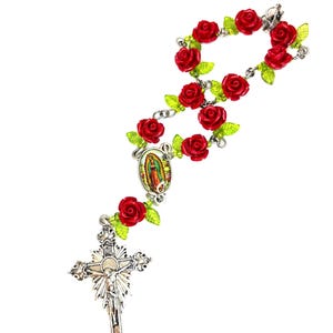 Op de afbeelding: Een rozenkrans met rode rozenkralen en groene bladeren. De rozenkrans heeft een zilveren kruisbeeld en een centrale hanger met een religieuze afbeelding. De kralen zijn verbonden door een zilveren ketting.