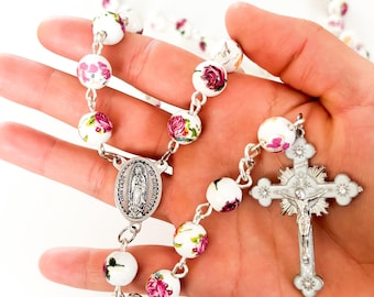 May include: White rosary beads with floral designs and a silver crucifix and Our Lady of Guadalupe medal.