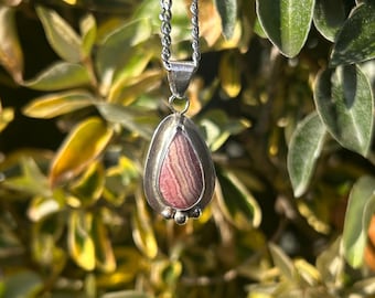 May include: A silver chain necklace with a teardrop-shaped pendant featuring a pink and white striped stone.