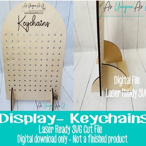 Pu&ograve; includere: Un espositore in legno per portachiavi. Il supporto in legno chiaro presenta numerosi piccoli fori per appendere i portachiavi. La parola "Keychains" &egrave; scritta in corsivo in alto. File SVG pronto per il laser.