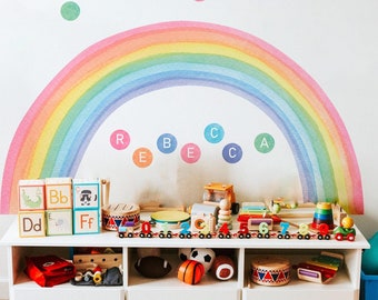 May include: A playroom scene with a white cabinet filled with toys, including wooden blocks, a toy train set, and sports balls. A rainbow wall decal and colorful polka dots decorate the white wall. A small chalkboard easel is on the left.