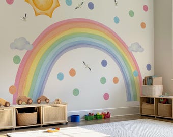 May include: A wall decal set featuring a large watercolor rainbow, a yellow sun, fluffy clouds, flying seagulls, and scattered multicolored polka dots. The design is applied to a plain wall above low wooden storage units with woven baskets.