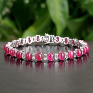 May include: A silver tennis bracelet with oval-shaped pink gemstones and smaller clear gemstones.