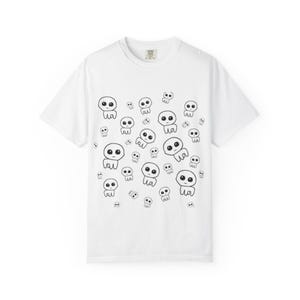 May include: White t-shirt with a repeating pattern of black cartoon figures. Each figure has large eyes and a small body. The figures are scattered across the shirt. The t-shirt has a crew neck and short sleeves.