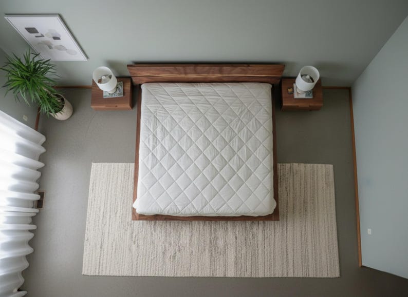 K&ouml;nnte beinhalten: Draufsicht auf ein Schlafzimmer mit einem Holzrahmenbett und einer wei&szlig;en, gesteppten Bettdecke. Zwei Nachttische mit Lampen flankieren das Bett. Ein strukturierter Teppich liegt am Fu&szlig; des Bettes, mit einer Topfpflanze und Kunstwerken.