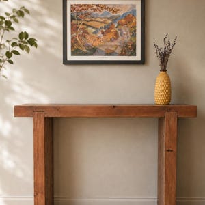 May include: A rustic, wooden console table with a framed landscape print and a yellow textured vase. The table is made of thick, solid wood and has a natural finish. The print features a colorful landscape scene, and the vase holds dried lavender.