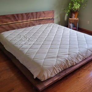 K&ouml;nnte beinhalten: Ein modernes Holzbettgestell mit einem Kopfteil aus Naturholz und einem niedrigen Profil. Das Bett ist mit einer wei&szlig;en, gesteppten Matratze bedeckt. Der Raum hat Hartholzb&ouml;den und eine gr&uuml;ne Wand.