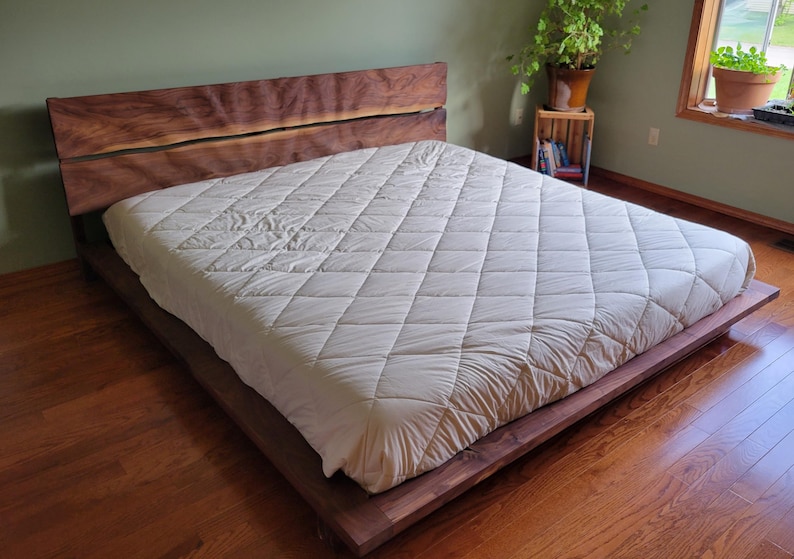 K&ouml;nnte beinhalten: Ein modernes Holzbettgestell mit einem Kopfteil aus Naturholz und einem niedrigen Profil. Das Bett ist mit einer wei&szlig;en, gesteppten Matratze bedeckt. Der Raum hat Hartholzb&ouml;den und eine gr&uuml;ne Wand.