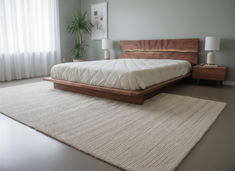 K&ouml;nnte beinhalten: Ein modernes Schlafzimmer mit einem niedrigen Holzrahmenbett und einem Kopfteil aus Naturholz. Das Bett ist mit einer wei&szlig;en, gesteppten Bettdecke bedeckt. Ein cremefarbener Teppich liegt auf dem Boden. Ein Nachttisch mit einer Lampe steht neben dem Bett. Das Bett ist ca. 200 cm lang.