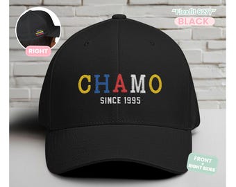 May include: Black baseball cap with the word "CHAMO" embroidered in yellow, red, and blue, with "SINCE 1995" underneath. The cap has a curved brim and a structured fit. The text "Flexfit 6277" and "BLACK" are also visible.