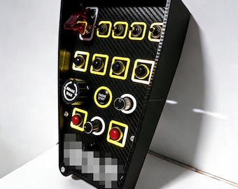 Puede incluir: Una caja de botones de carreras negra con una placa frontal de textura de fibra de carbono, que cuenta con múltiples interruptores de palanca, botones pulsadores y diales giratorios. El panel incluye una cubierta de seguridad roja y un botón de arranque.