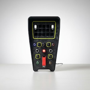 Op de afbeelding: Een zwarte elektronische bedieningsconsole met een trapeziumvorm, voorzien van een raster van vierkante uitsparingen aan de bovenkant met een neongele omlijning. Het paneel bevat diverse draaiknoppen, een centrale rode knop en een rode hendel.