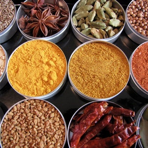 May include: Assortment of spices in small metal containers. The spices include cumin seeds, star anise, cardamom pods, turmeric powder, curry powder, paprika, fenugreek seeds, and dried chili peppers.