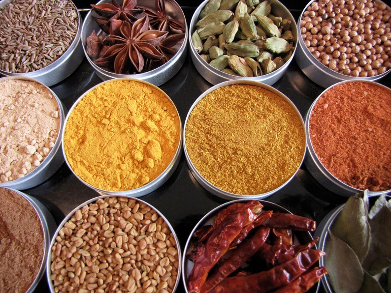 May include: Assortment of spices in small metal containers. The spices include cumin seeds, star anise, cardamom pods, turmeric powder, curry powder, paprika, fenugreek seeds, and dried chili peppers.