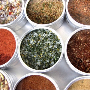 Peut inclure: Une collection de huit petits récipients ronds en argent remplis de diverses épices et herbes. Les épices sont de couleur rouge, brune, verte et blanche.