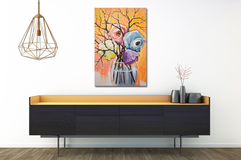 Op de afbeelding: Een schilderij van een boeket kleurrijke bloemen in een heldere glazen vaas. De bloemen zijn roze, blauw, paars en geel. De achtergrond is een warme oranje kleur met witte bloesems.