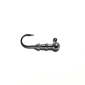 May include: A silver fishing jig with a round head and a hook. The jig has a textured body.