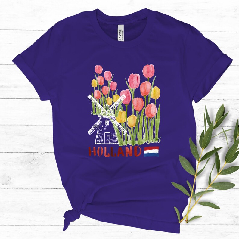 May include: Purple t-shirt featuring a white windmill and red, yellow, and pink tulips. The shirt also has the word "HOLLAND" and the Dutch flag printed on it.