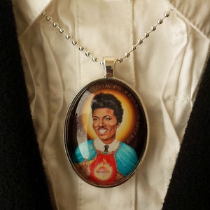 May include: A silver chain necklace with a round pendant featuring a portrait of a man with a heart-shaped design. The pendant has the text "WOP BOP ALOO MOPALOP BAM BOOM" around the edge.