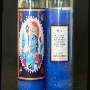 May include: Two blue glass candle jars with a blue wax interior. The left jar has a label with an image of a blue-skinned deity playing a flute. The label text reads "MJK Meditation: Holy Mother, Full of Grace... Please give Michael a brand new face. &copy; 1992 by Vicki Berndt www.vickiberndt.com".