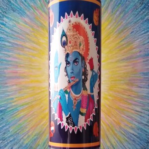 May include: A blue glass candle with a colorful image of a person with a crown and a flute. The image is surrounded by a white and pink border with a blue background.