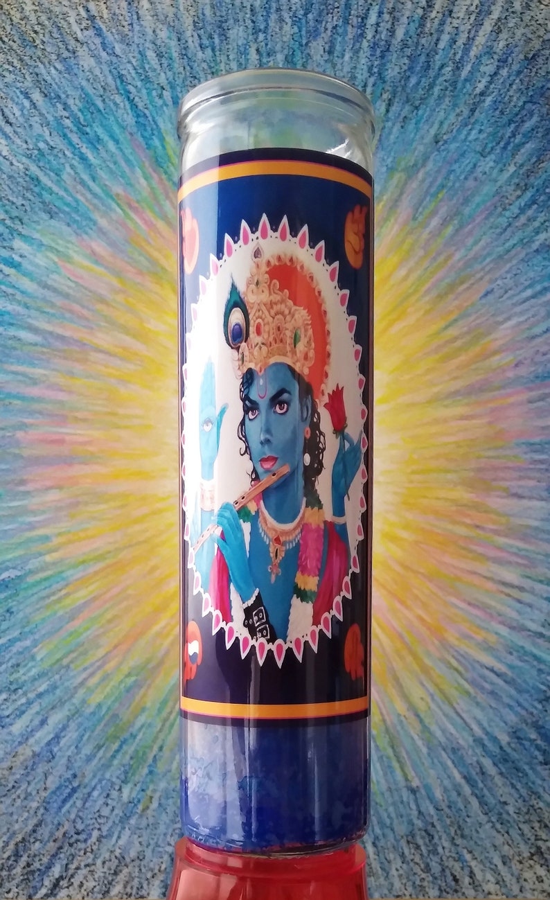 May include: A blue glass candle with a colorful image of a person with a crown and a flute. The image is surrounded by a white and pink border with a blue background.