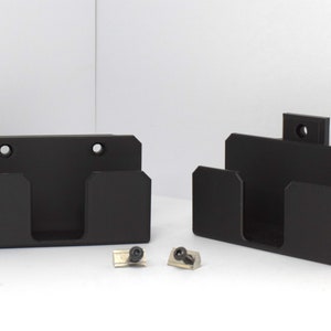 May include: Two black wall-mounted organizers with three compartments each. The organizers are made of plastic and have a matte finish. They are designed to hold small items, such as tools or craft supplies. The organizers come with two screws and two wall anchors.