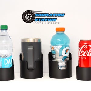 May include: Four black cup holders with different beverages inside. The holders are mounted on a white surface. The beverages include a clear water bottle, a blue sports drink, a gray travel mug, and a red can of Coca-Cola.