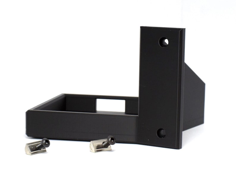 May include: Black, L-shaped bracket with a rectangular base and vertical support, featuring two pre-drilled holes. Two small, silver-colored screws are included. The bracket is designed for mounting and support.