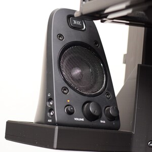 May include: Black computer speaker with a mesh grill and volume and bass control knobs. The speaker has the text "THX" at the top and "VOLUME" and "BASS" below the knobs. An orange light is illuminated.