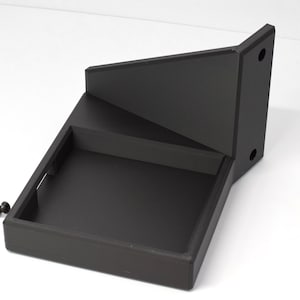 May include: A black, geometric wall-mounted shelf with a stepped design. The shelf has a rectangular base, a middle shelf, and an angled top section. Two silver cufflinks are placed near the shelf.