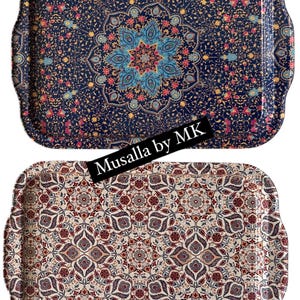 May include: Two decorative serving trays with intricate floral patterns. The top tray has a blue background with gold and pink accents. The bottom tray has a cream background with red, blue, and gold accents. Both trays feature the text "Musalla by MK". The top tray is labeled "Eymen" and the bottom tray is labeled "Belma".