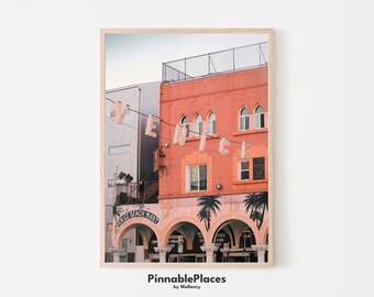 May include: A photograph of a building in Venice Beach, California. The building is painted a light orange color and has a sign that reads "Venice Beach Mart". There are palm trees in front of the building and a sign that reads "Venice" in large letters.
