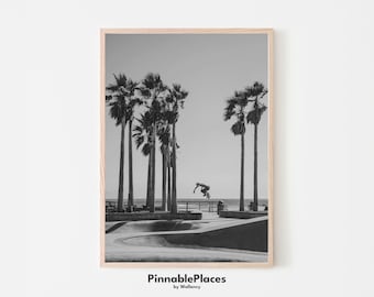 May include: Black and white photograph of a skateboarder performing a trick in a skate park with palm trees in the background. The image is framed with a light wood frame. The text "PinnablePlaces by Wallency" is at the bottom of the image.