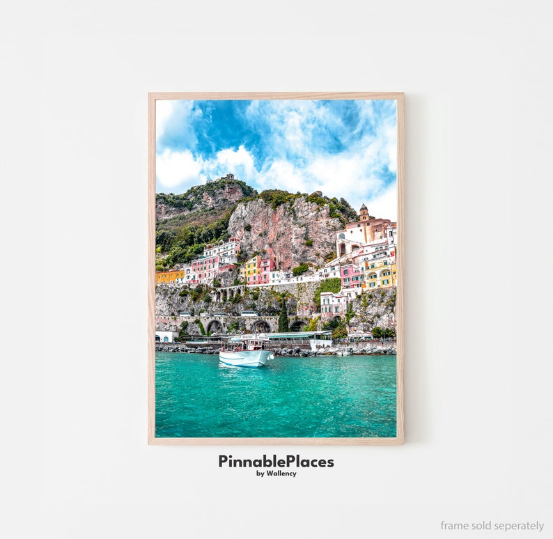 May include: A colorful town built into a cliffside overlooking a turquoise bay with a white boat in the water. The sky is blue with white clouds. The text "PinnablePlaces by Wallency" is at the bottom of the image.