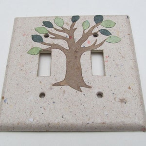 Peut inclure: Une plaque de prise double en céramique beige clair avec une silhouette d'arbre brune et des feuilles vertes. La plaque a une texture mouchetée.