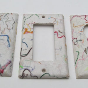 May include: Three decorative light switch covers. Each cover is white with colorful, squiggly lines in red, blue, green, and yellow. The covers are for a single switch, a double switch, and an outlet.