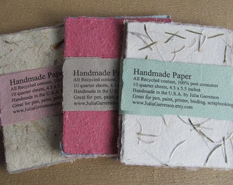 Puede incluir: Tres pilas de papel hecho a mano, cada una de un color diferente: blanco, rosa y verde claro. El papel está hecho con contenido reciclado y es ideal para bolígrafo, pintura, impresión, encuadernación y scrapbooking. La etiqueta en la pila blanca dice: "Handmade Paper, All Recycled content, 100% post consumer, 10 quarter sheets, 4.5 x 5.5 inches, Handmade in the U.S.A. by Julia Garretson, Great for pen, paint, printer, binding, scrapbooking, www.JuliaGarretson.etsy.com".