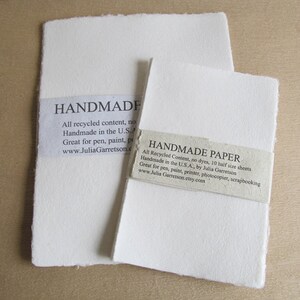 May include: Two sheets of handmade paper, both white and textured. The larger sheet has a label that reads "HANDMADE" and "All recycled content, no dyes. Handmade in the U.S.A. Great for pen, paint, printer, photocopier, scrapbooking. www.JuliaGarretson.etsy.com". The smaller sheet has a label that reads "HANDMADE PAPER" and "All Recycled Content, no dyes, 10 half size sheets. Handmade in the U.S.A., by Julia Garretson. Great for pen, paint, printer, photocopier, scrapbooking. www.JuliaGarretson.etsy.com".